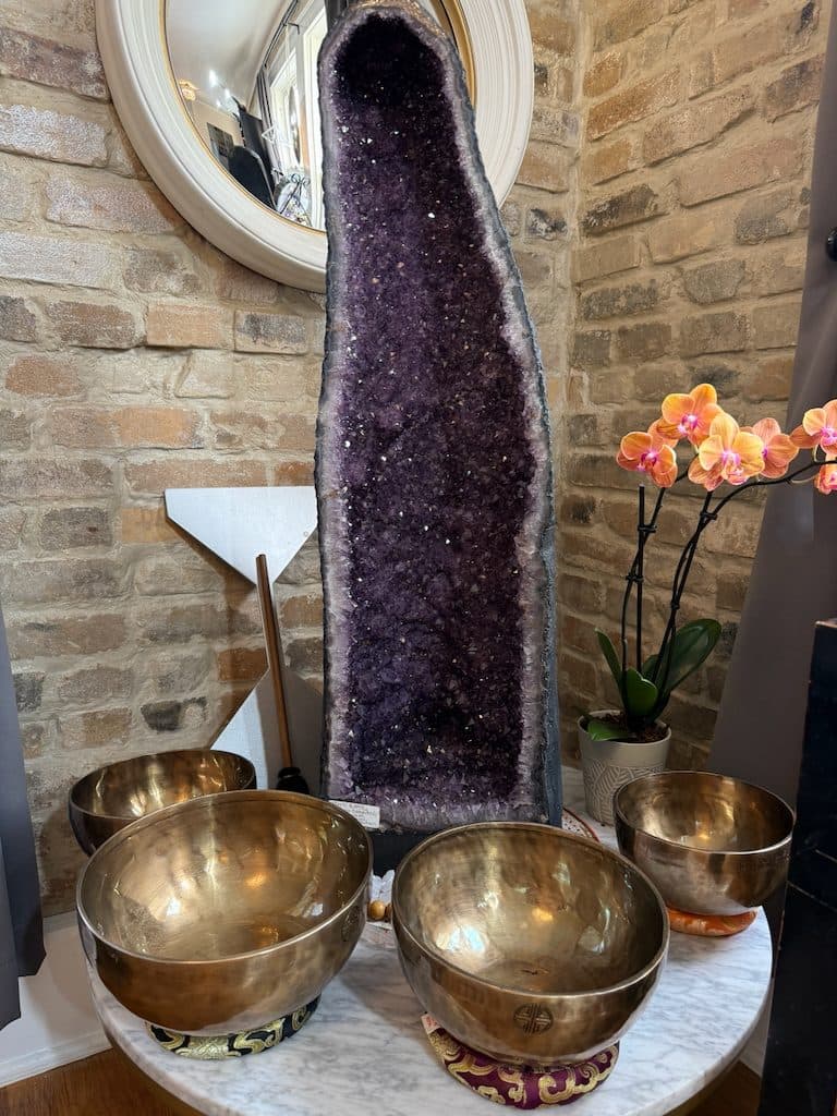 Tall amethyst geode cathedral beside brass singing bowls and an orange orchid